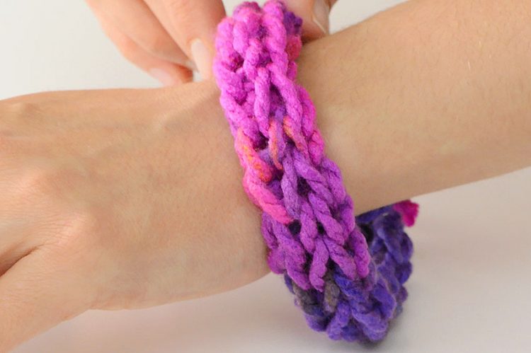 A wrist wearing a multicoloured finger knitted bracelet