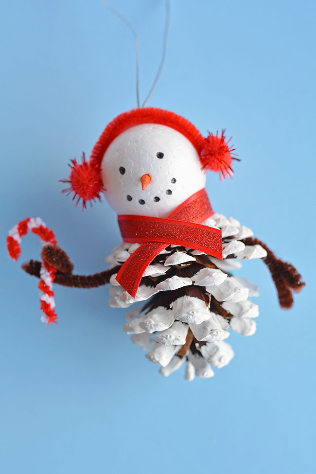 These pinecone snowman ornaments are so FUN and look super cute hanging from the tree! Such a fun Christmas craft for kids of all ages! Using dollar store supplies you can transform a regular old pinecone into a little bundled-up snowman complete with a top hat, scarf and earmuffs! It's a great homemade Christmas ornament you can pull out year after year. Or you can leave it up all winter long as a frosty decoration!