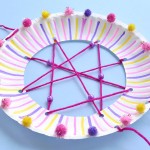 Dreamcatcher decorated with pom poms sitting on a blue background