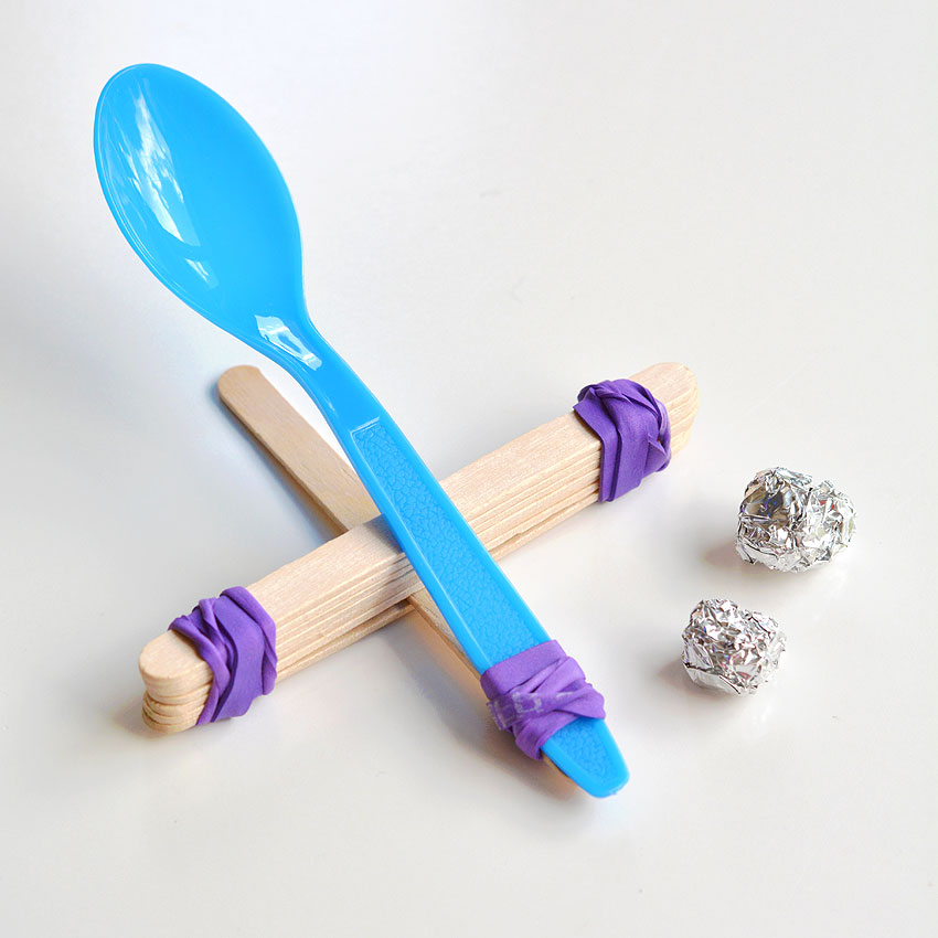 A popsicle stick catapult with tin foil balls beside it