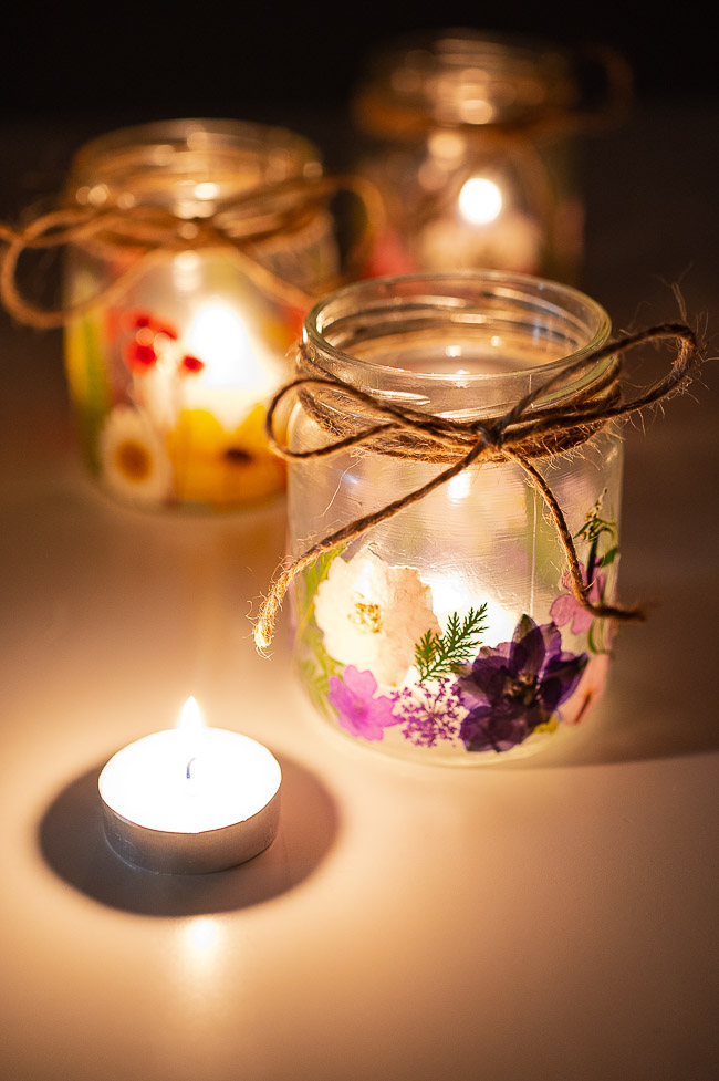 Three pressed flower lanterns, one in front with a lit tealight beside it