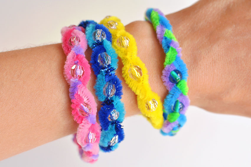 Four different colors of braided pipe cleaner bracelets on a wrist