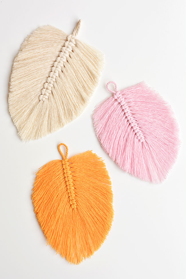 Three colours of macrame feathers on a white background