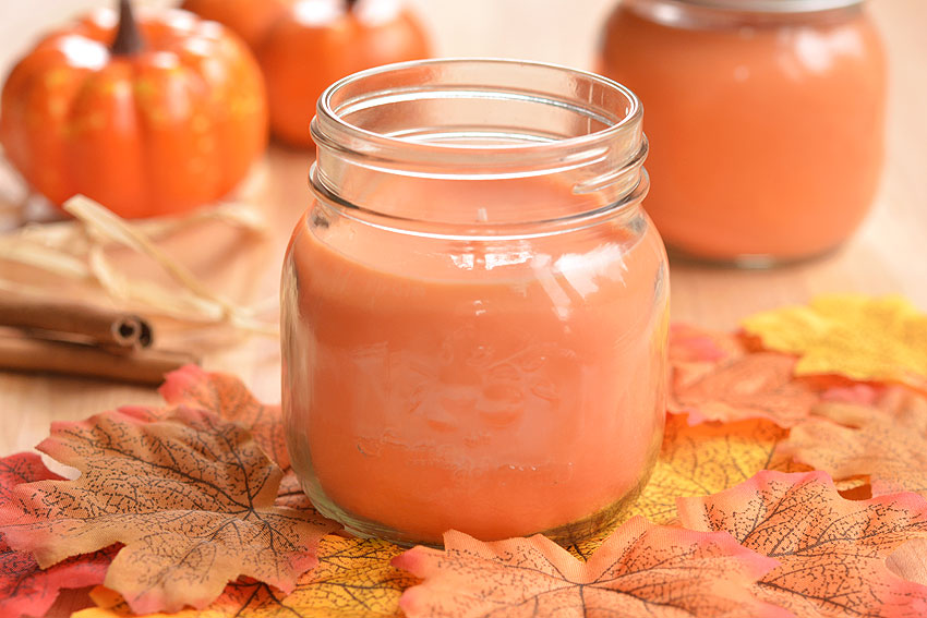 DIY pumpkin spice candle surrounded by fall leaves, pumpkins, and cinnamon sticks