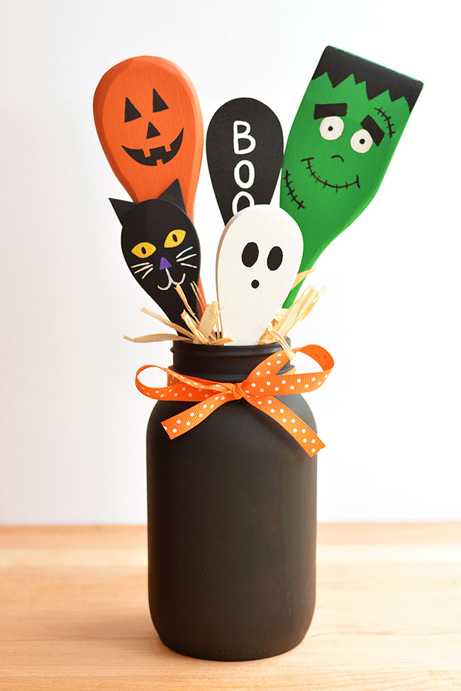 Halloween painted wooden spoons in a black mason jar with orange ribbon tied around it