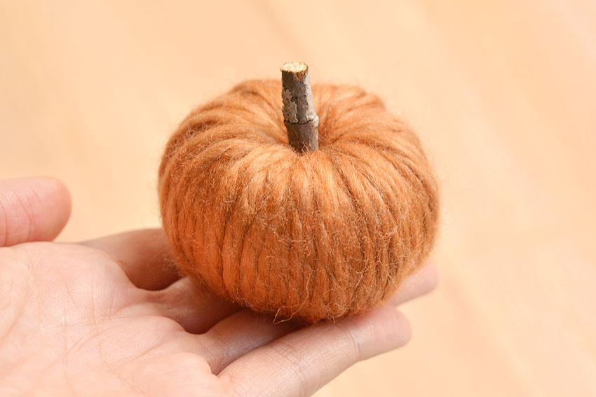 A yarn pumpkin held on fingertips