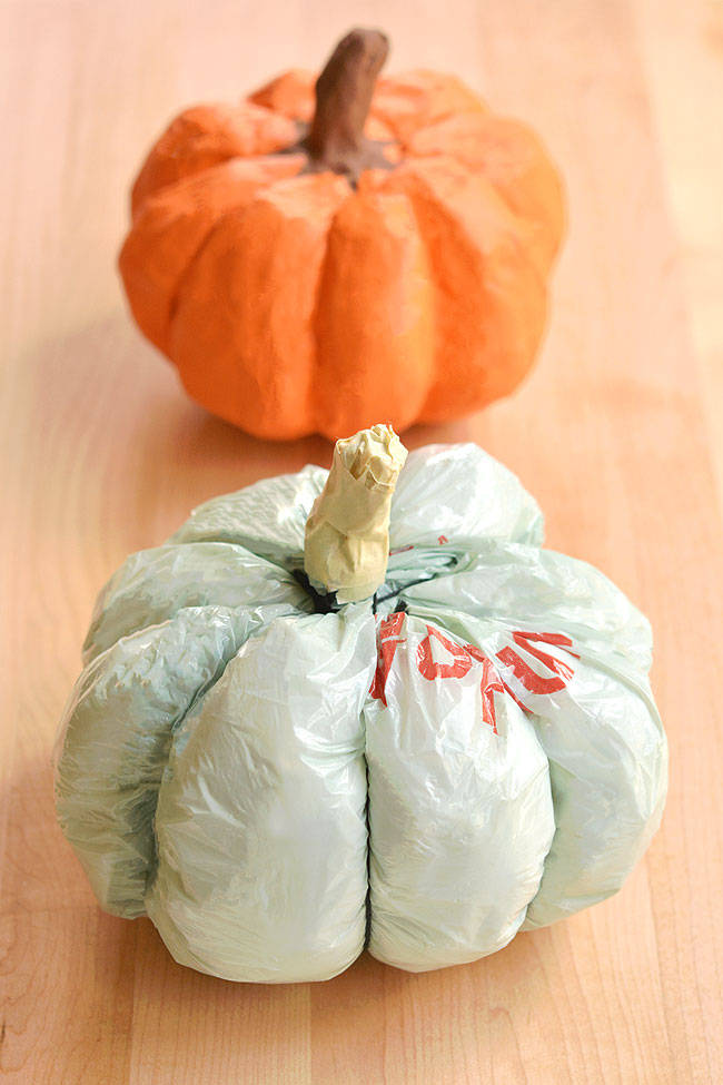 A finished pumpkin made of paper mache beside the grocery bag pumpkin shape