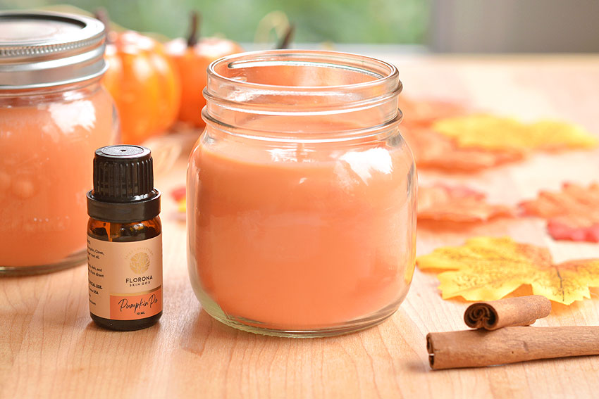 Spiced pumpkin scented candle on a wood surface with leaves, cinnamon sticks, and an essential oil bottle