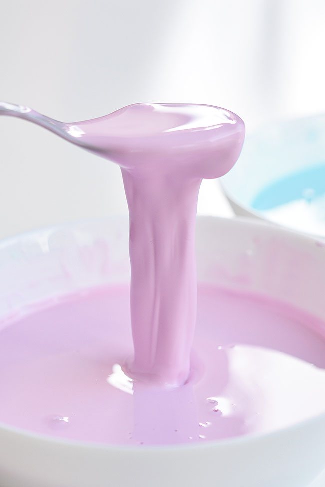 Purple oobleck coming off a spoon into a bowl