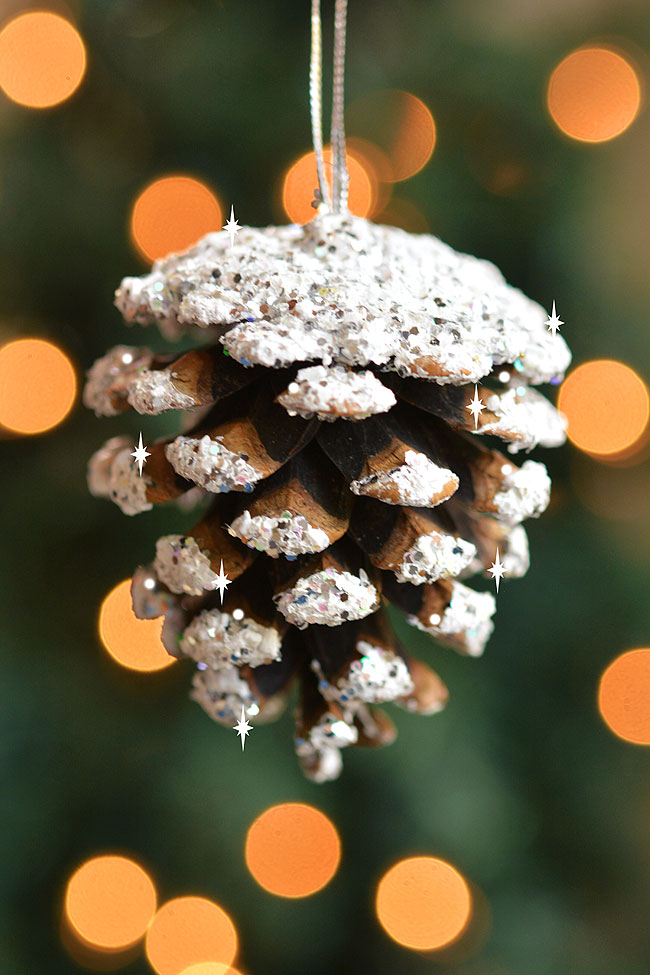 Frosted pine cone hanging in front of Christmas tree lights