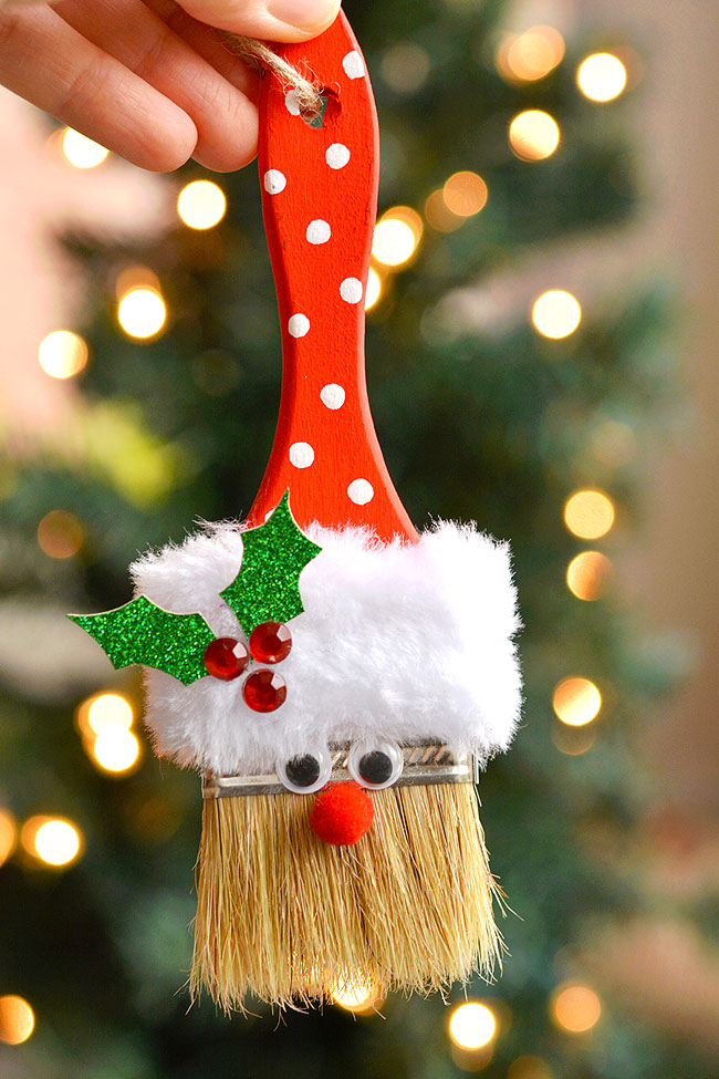 Paint brush Santa ornament held in front of a Christmas tree