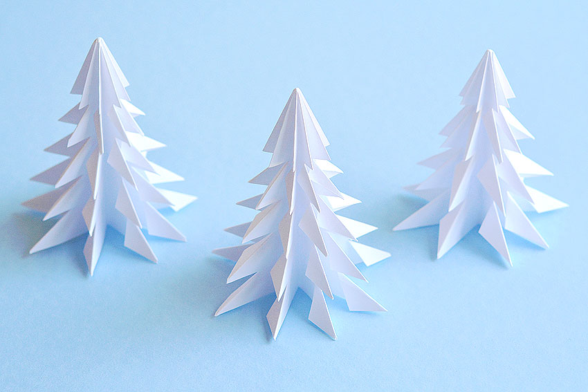 Three paper Christmas trees on a blue background
