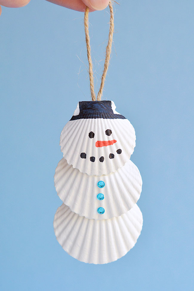 Seashell snowman ornament hanging in front of a blue background