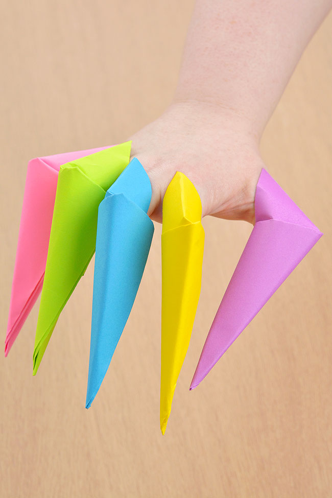 A hand wearing five different colours of paper claws