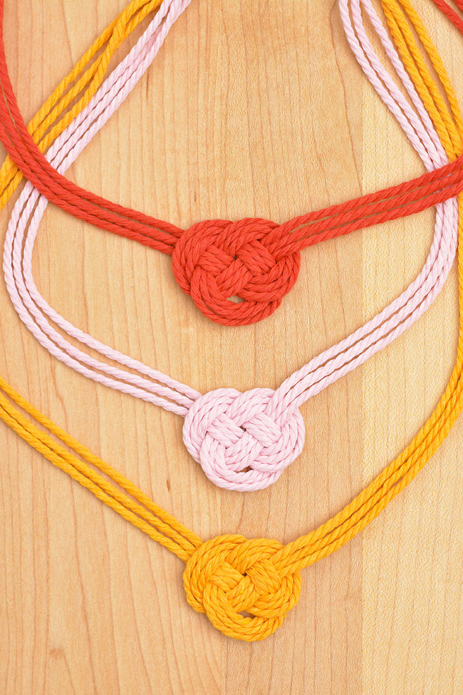 Three Celtic heart macrame necklaces on a wooden background