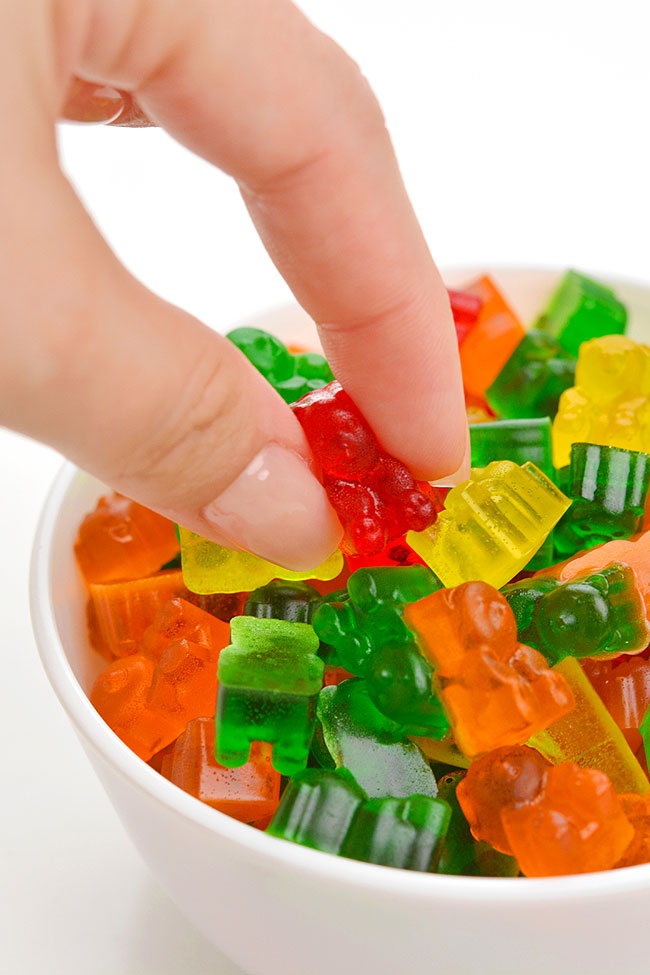 Squishing a red gummy bear above a bowl of homemade gummy bears