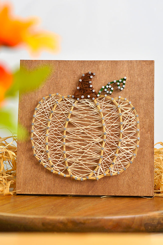 Cream coloured pumpkin string art on a stained wood board