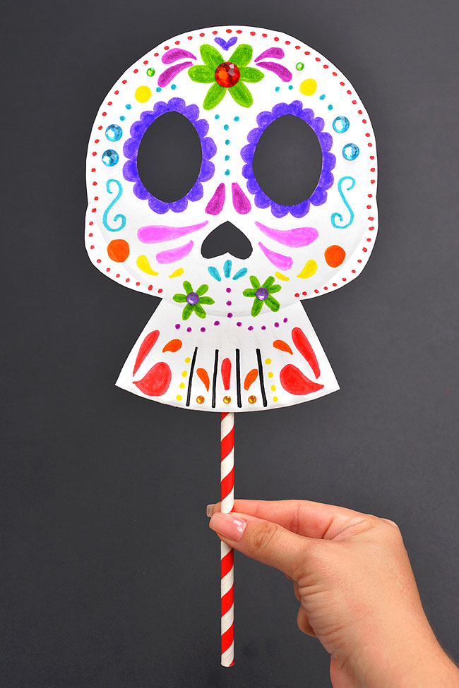 Holding a Día de los Muertos mask with a sugar skull design