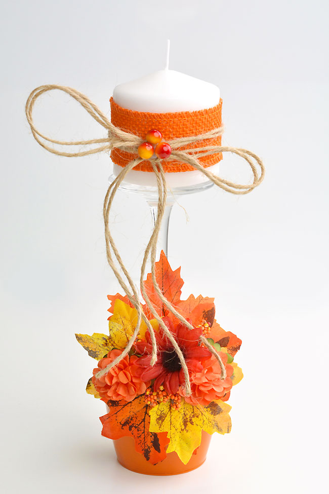 Wine glass candle holder decorated with fall leaves, flowers, and twine