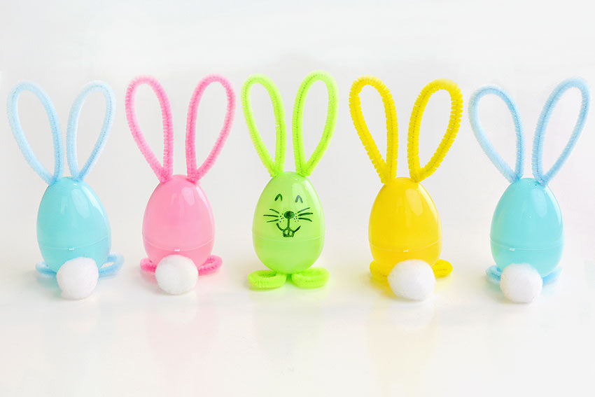 Row of bunny plastic eggs with 4 facing backwards showing their fluffy tails and 1 facing forward