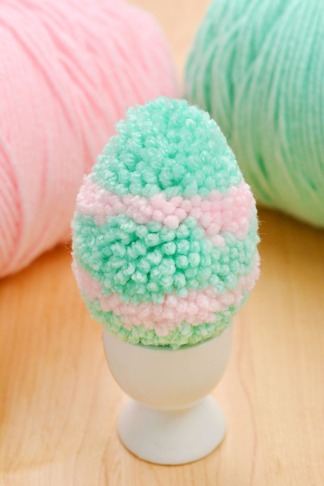 Green and pink Easter egg pom pom sitting in an egg cup