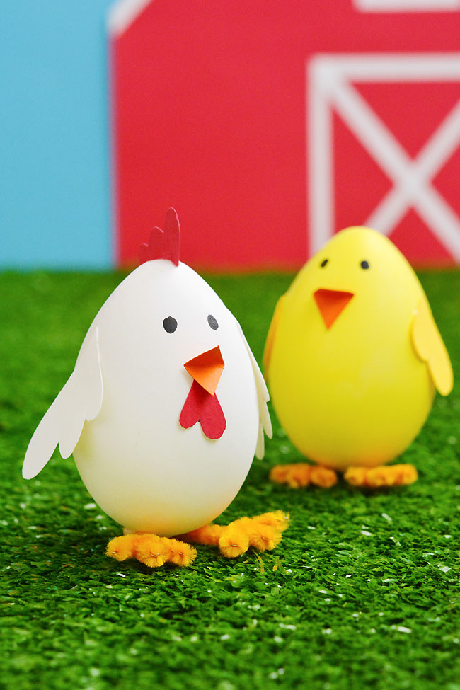 Easter eggs decorated like a chick and chicken in front of a barn