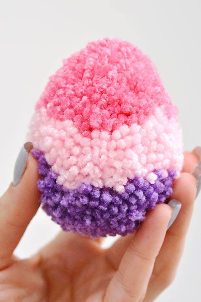 Holding a fluffy pink and purple pom pom Easter egg