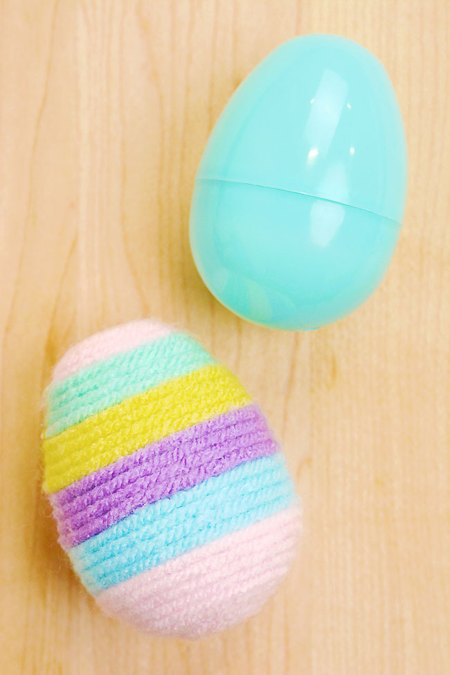 A plastic egg with a yarn wrapped egg beside it