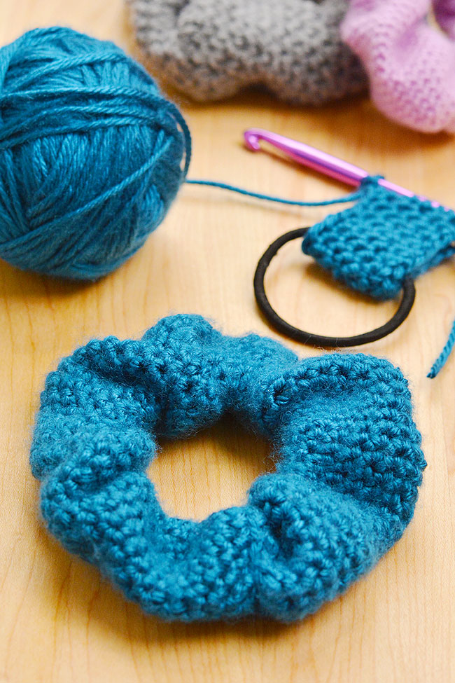 Teal scrunchie on a wood background with yarn and a crochet hook