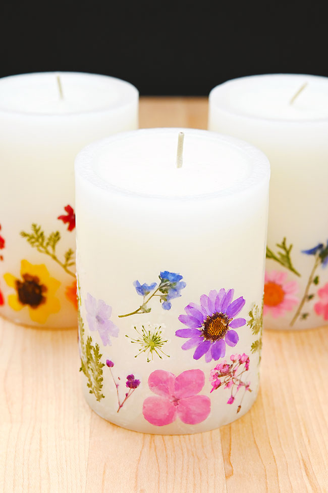 Pressed dried flowers decorating the side of 3 white pillar candles