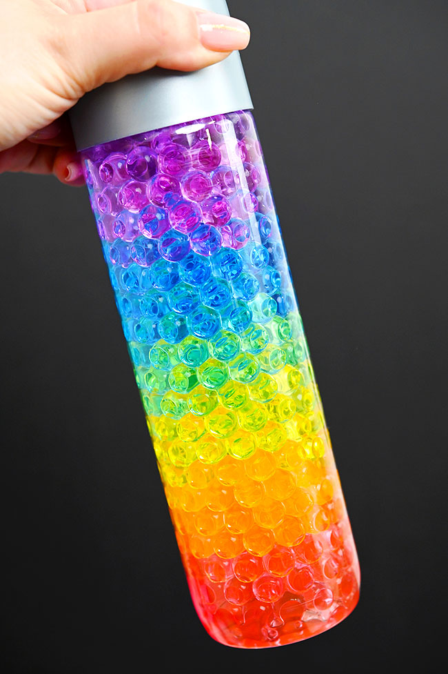 Holding a rainbow sensory bottle made with water beads