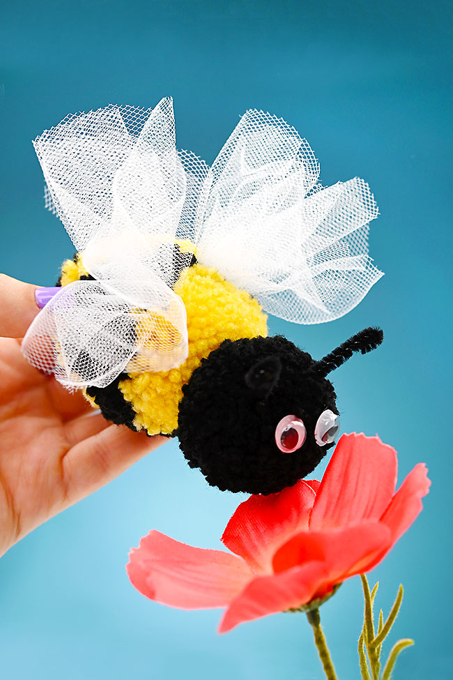 Holding a bee pom pom craft by a flower