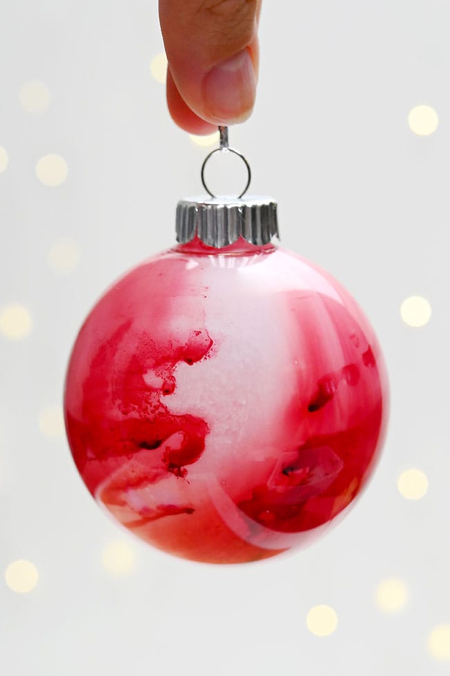 Alcohol Ink Christmas Ornaments Holding a red Christmas ornament decorated with alcohol ink