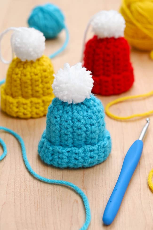 Crochet Beanie Ornament Crochet beanie ornaments on a wooden background with yarn and a crochet hook
