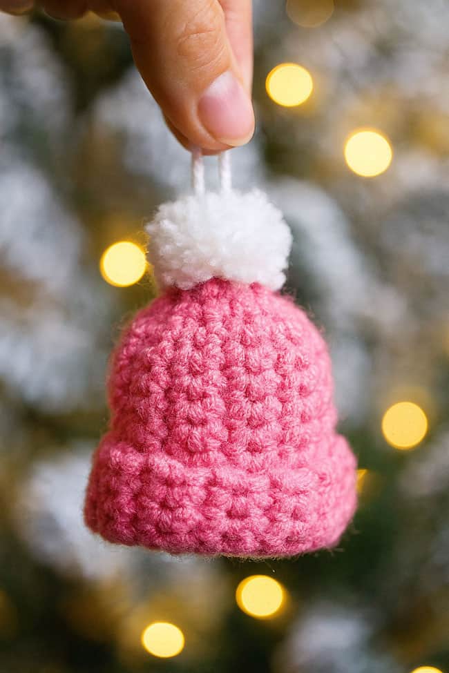 Crochet Mini Hat Ornament Holding a mini crochet hat ornament in front of the Christmas tree