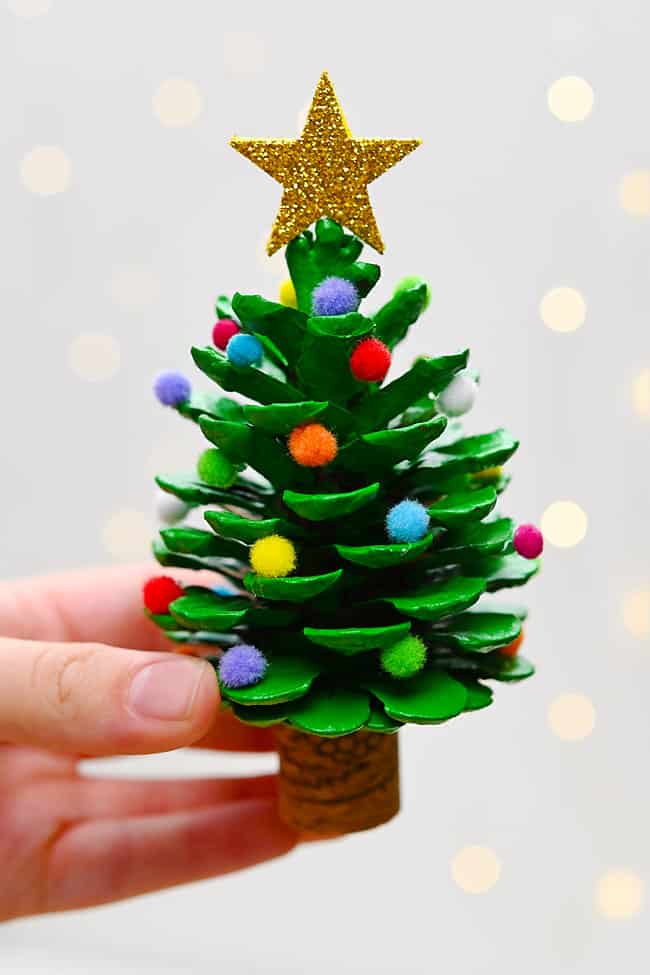 Holding a pine cone Christmas tree with a glitter star topper