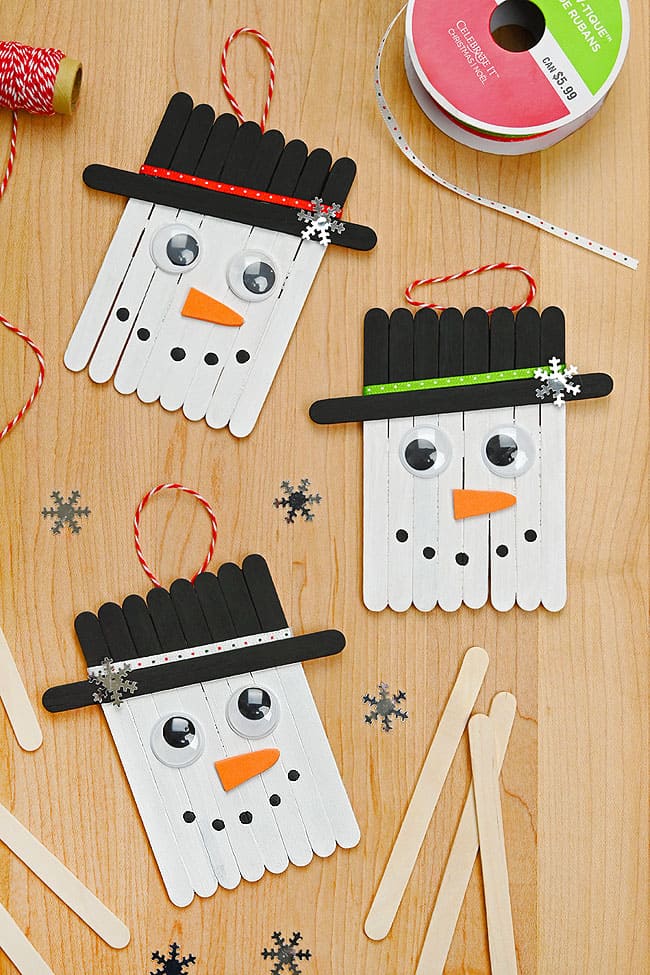 Snowman Craft with Popsicle Stick Snowman ornaments made with popsicle sticks on a wood background