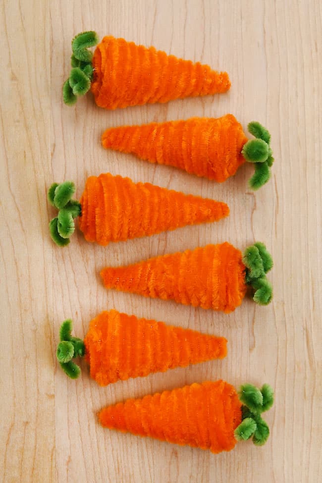 Carrot Pipe Cleaner Craft Easter pipe cleaner crafts lined up on a wood background