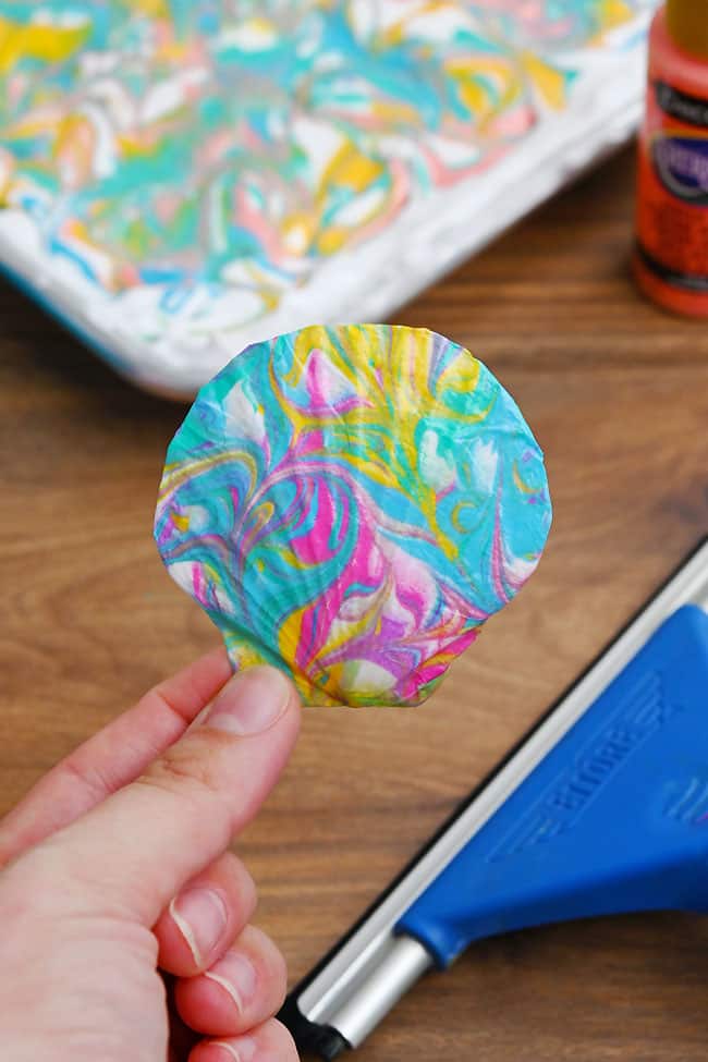 Shell Painting Ideas Holding a scallop shell decoupaged with blue, pink, purple, and yellow marbling