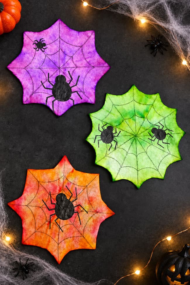 Coffee Filter Spider Suncatchers Purple, green, and orange coffee filter spiderwebs with black spiders on them
